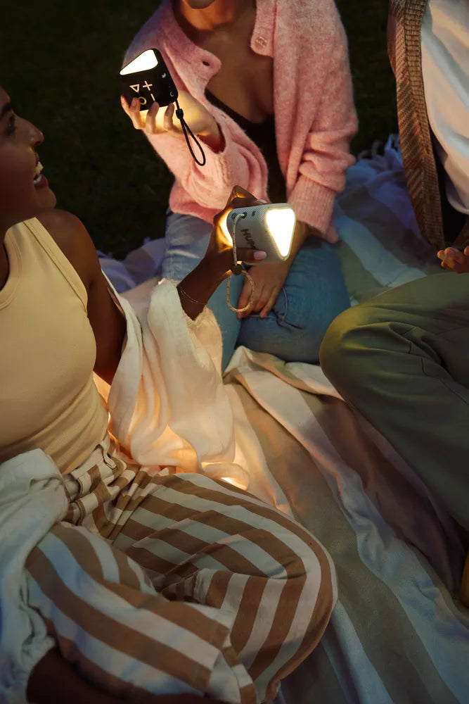 Two people sitting together, with 2 HUMM GLO Bluetooth speakers featuring mood lights, at a nighttime picnic.