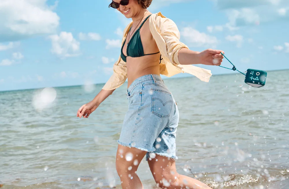 A woman walking on a beach with a waterproof HUMM GLO Bluetooth speaker.